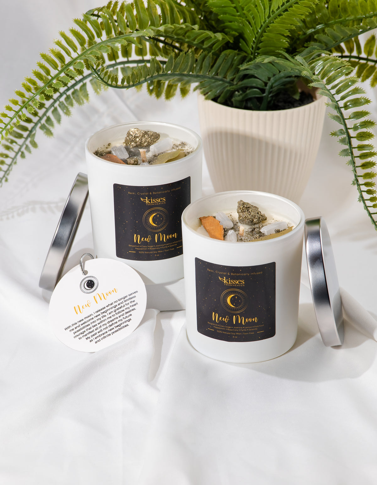 Two candles with decorative elements on a white surface with a fern in the background