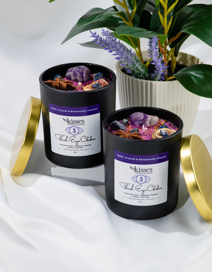 Two black candles with gold lids on a white surface, surrounded by plants.