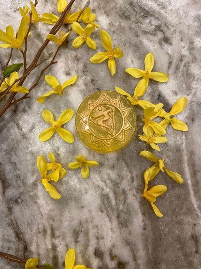 Gold button with a symbol surrounded by yellow flowers on a marble surface