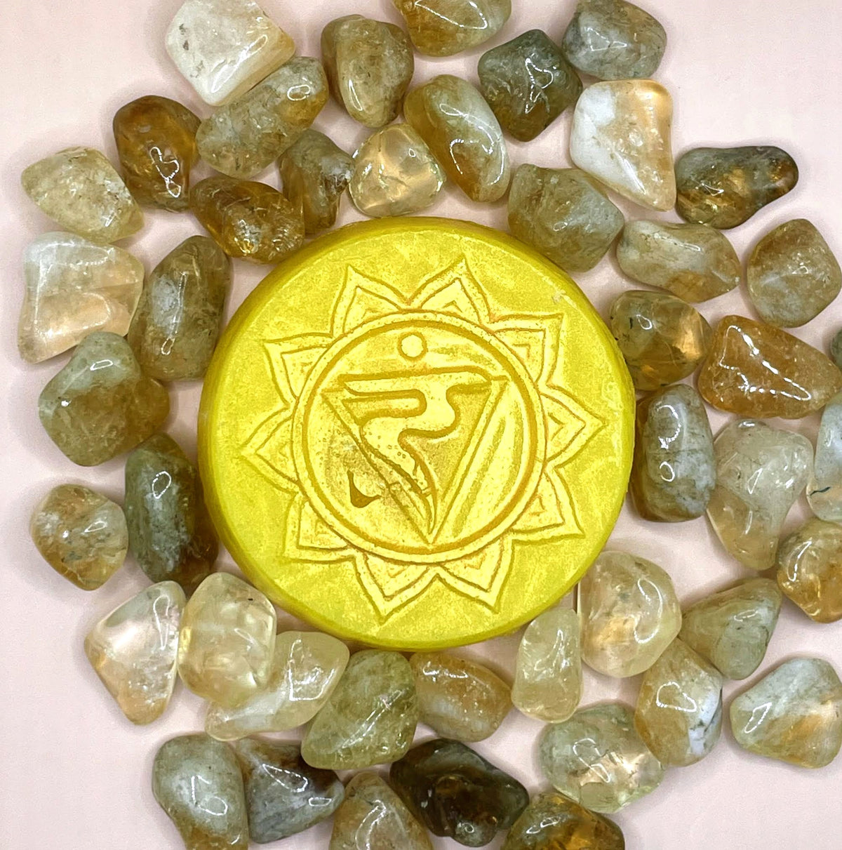 Yellow circular object with a symbol surrounded by green stones on a light pink background
