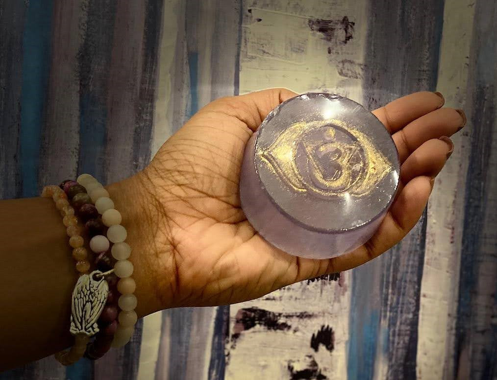 Hand holding a round, translucent object with gold designs against a patterned curtain background