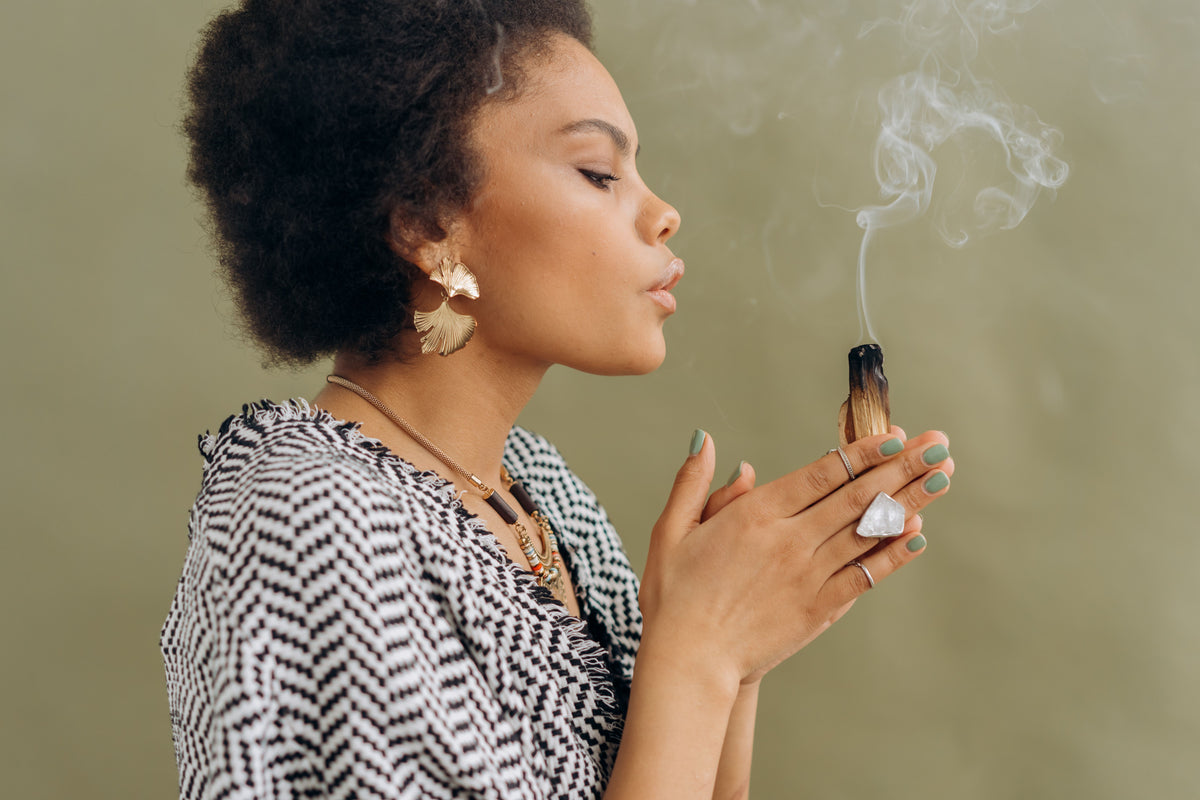 Woman holding a lit cigarette with smoke against a plain background